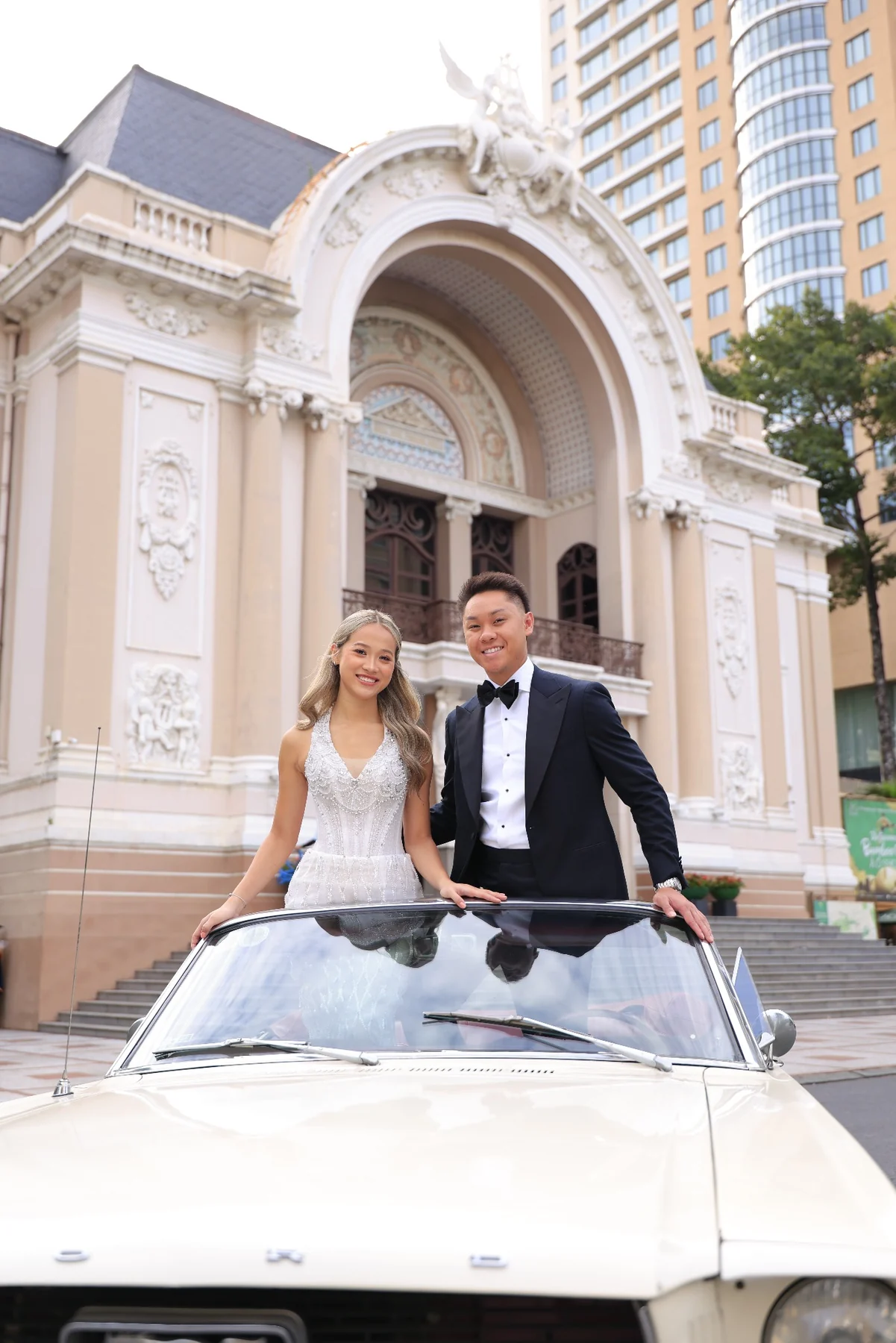 Huyen and Ryan standing with a vintage white Mustang